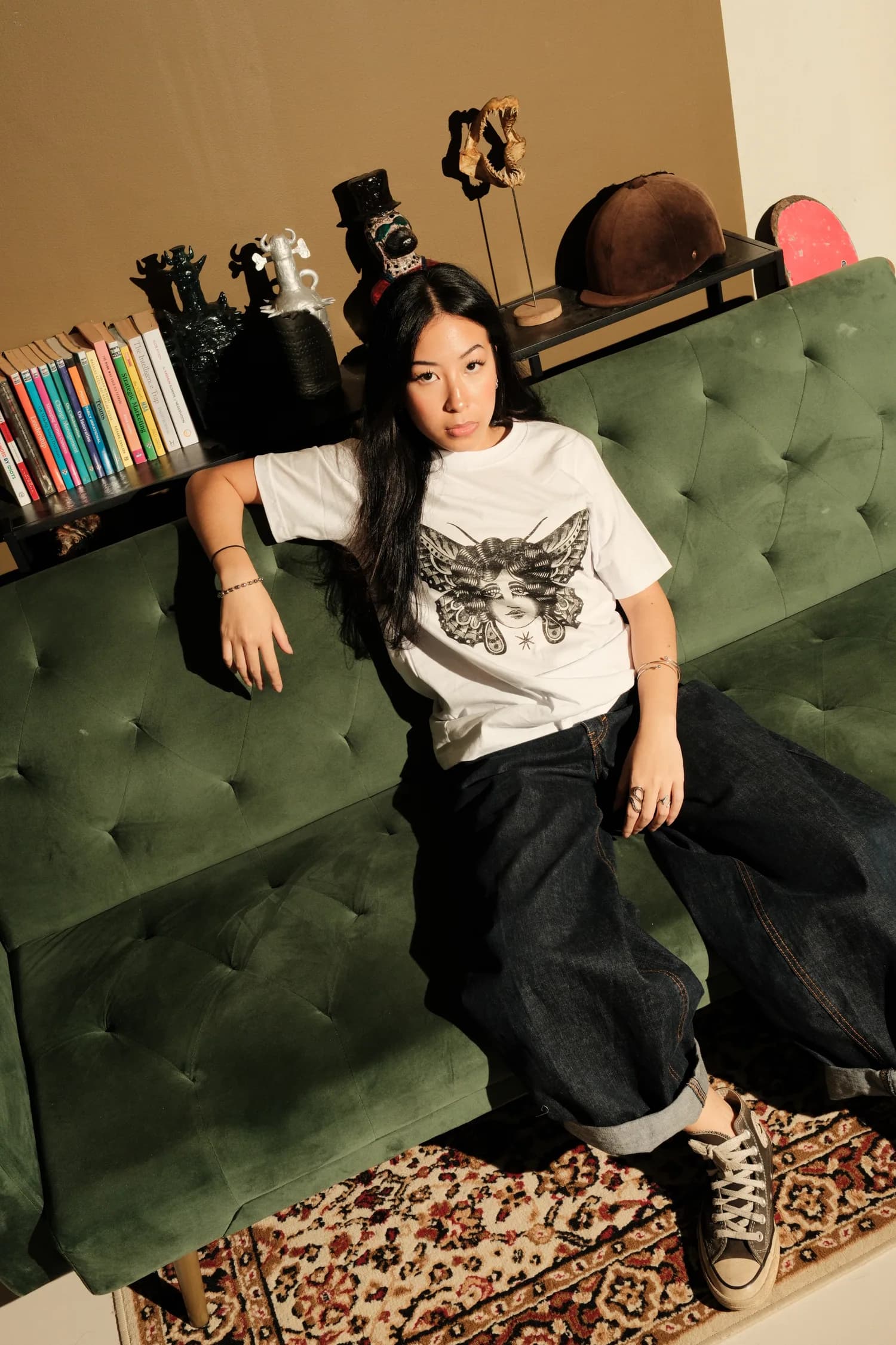 Model in a white TOHO Visage T-shirt seated in a green armchair.