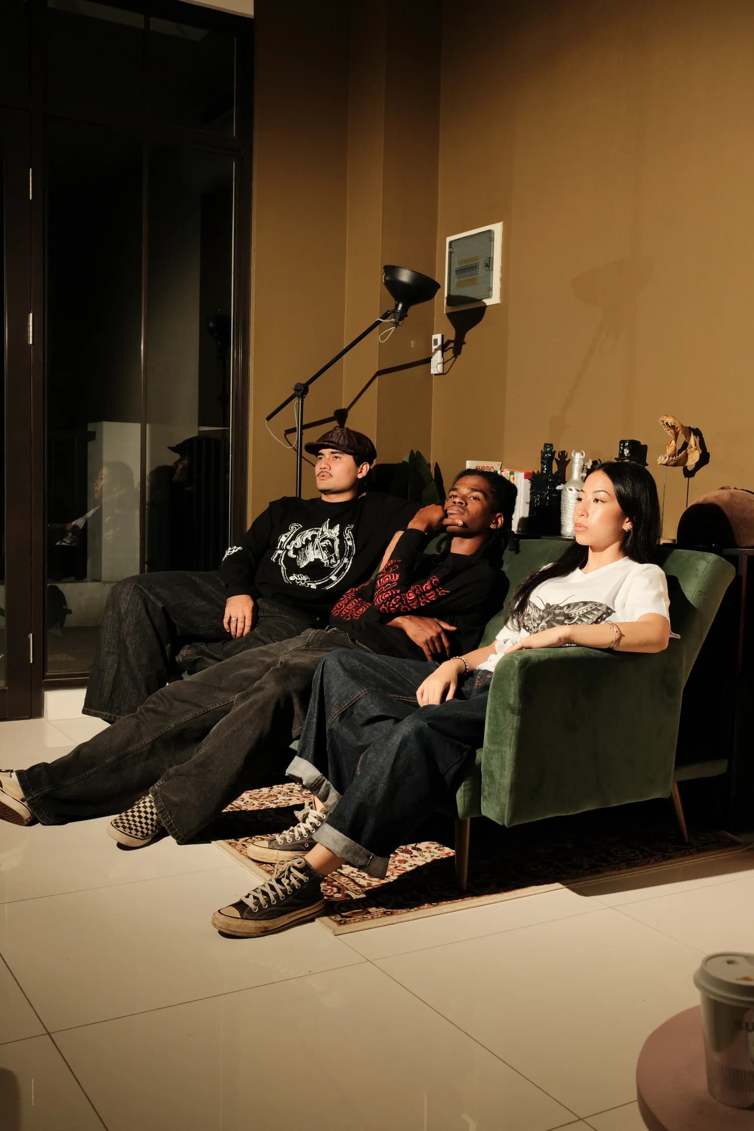 Three models in TOHO graphic pieces seated together in a warmly lit interior.